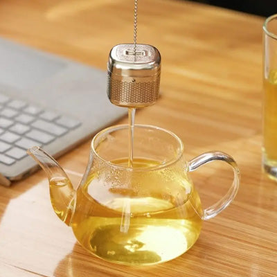 infuseur thé au dessus de théière près ordinateur sur bureau